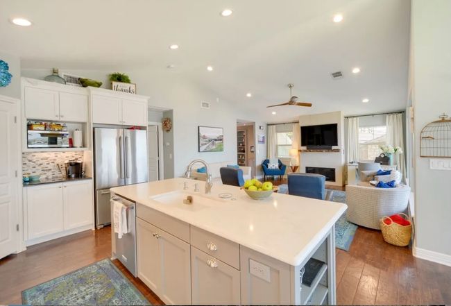 Kitchen with stainless steel appliances, dark wood finished floors, white cabinetry, ceiling fan, and an island with sink | Image 4