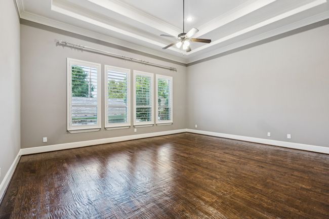 Unfurnished master bedroom featuring a raised ceiling, ornamental molding, ceiling fan, dark wood-style floors, and baseboards | Image 16