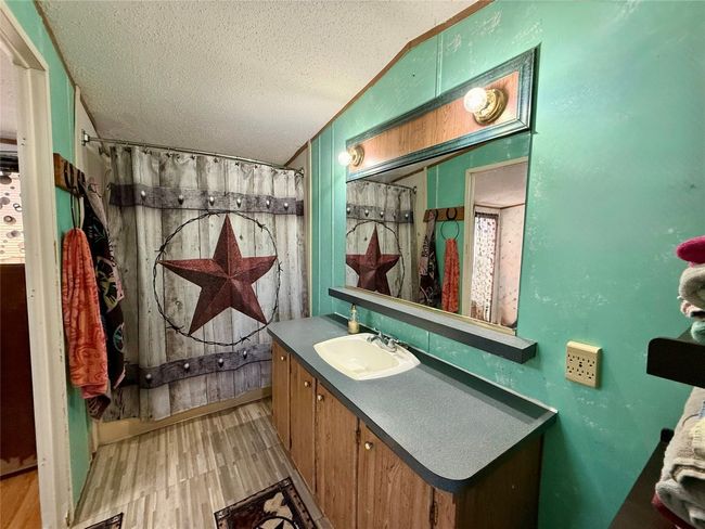 Full bath featuring a textured ceiling, curtained shower, wood finished floors, vanity, and vaulted ceiling | Image 13