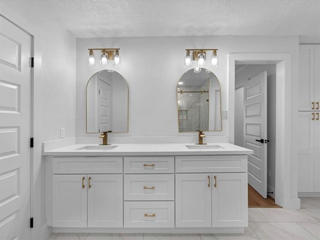 This modern bathroom features a double vanity with sleek white cabinetry and gold fixtures. It has two stylish mirrors, elegant lighting, and a clean, contemporary design with a neutral color palette. | Image 23