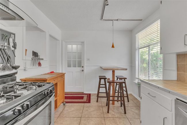 Kitchen featuring tile countertops, appliances with stainless steel finishes, light tile patterned flooring, white cabinetry, and decorative light fixtures | Image 8