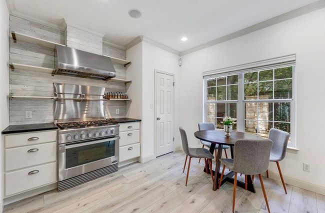 Kitchen with open shelves, stainless steel gas range, wall chimney exhaust hood, dark countertops, and ornamental molding | Image 14