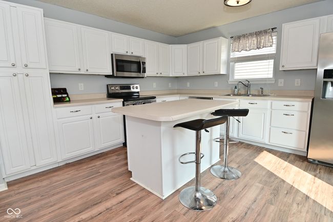 kitchen with stainless steel appliances, a sink, white cabinets, light wood-style flooring, and a kitchen bar | Image 18