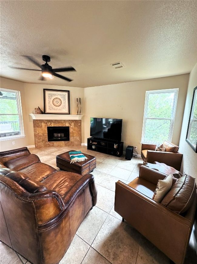 Living area with a textured ceiling, ceiling fan, a high end fireplace, and tile patterned floors. | Image 5
