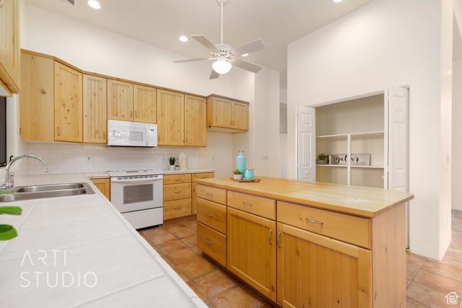 Kitchen with a sink, white appliances, a ceiling fan, tasteful backsplash, and butcher block counters | Image 18