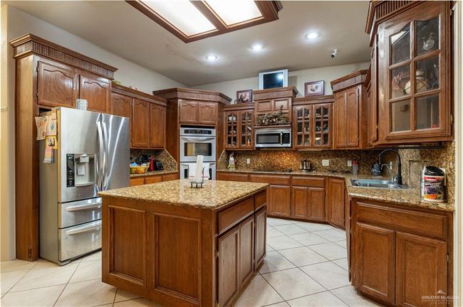 Kitchen with light stone countertops, sink, a kitchen island, stainless steel appliances, and decorative backsplash | Image 14