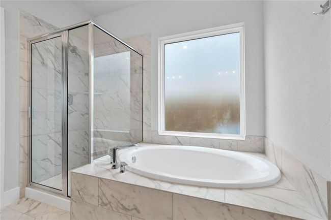 Additional view of this beautiful primary bathroom features a dark framed walk-in shower with tile surround, separate garden tub for soaking after a long day with custom tile detailing, high ceilings, custom paint, and a large tempered glass window for natural lighting. | Image 12