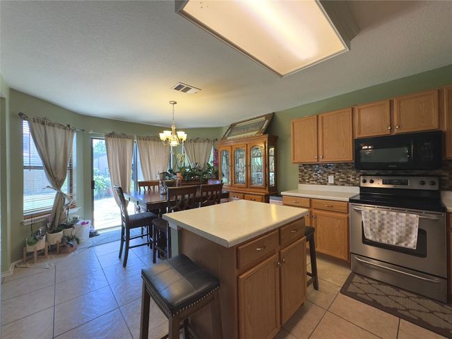 Kitchen featuring black microwave, stainless steel electric stove, a chandelier, light tile patterned floors, and backsplash | Image 10