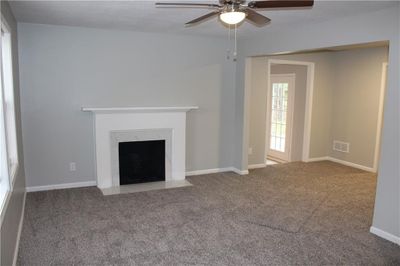 Unfurnished living room with carpet flooring, a fireplace, and ceiling fan | Image 2