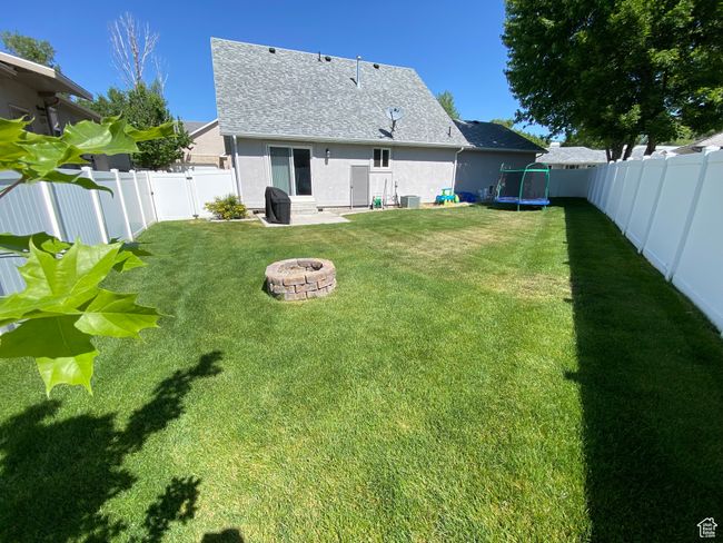 Back of house featuring a fire pit, a trampoline, stucco siding, roof with shingles, and central air condition unit | Image 26
