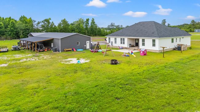 Back of property featuring a carport, a yard, an outdoor structure, and view of wooded area | Image 4