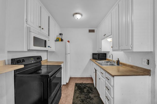 Kitchen with black appliances, wood finished floors, and white cabinets | Image 7