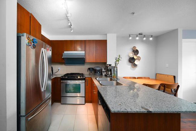 Kitchen with a peninsula, under cabinet range hood, brown cabinets, appliances with stainless steel finishes, and a sink | Image 4