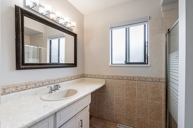 Bathroom with vanity, tile patterned flooring, tile walls, a tile shower, and a wainscoted wall | Image 15