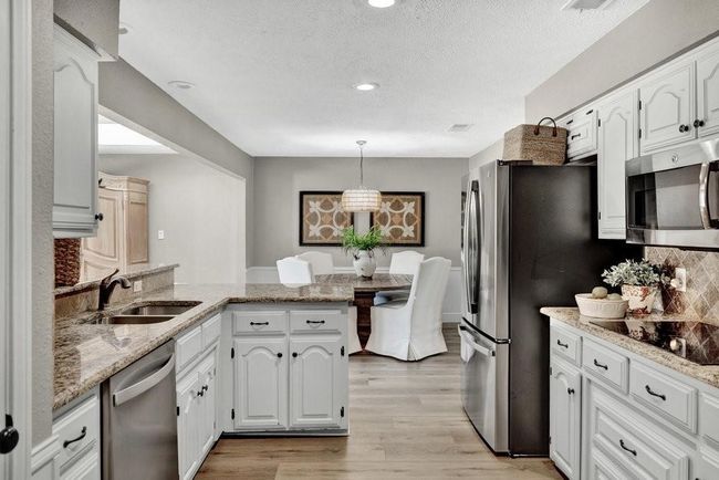 Kitchen featuring white cabinets, a peninsula, appliances with stainless steel finishes, a sink, and light wood-type flooring | Image 14