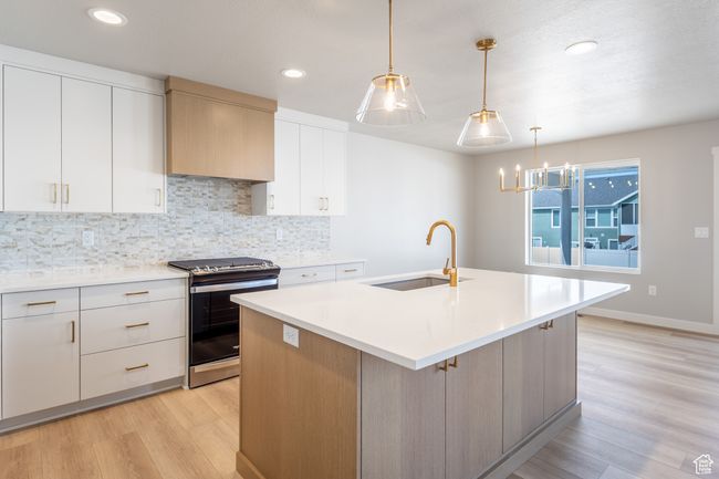 Kitchen featuring stainless steel gas stove, a sink, light wood finished floors, decorative backsplash, and light countertops | Image 9