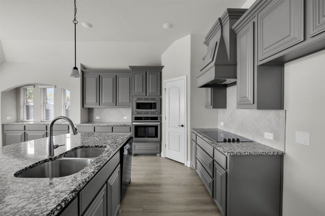 Kitchen featuring sink, light stone counters, backsplash, black appliances, and custom exhaust hood | Image 19
