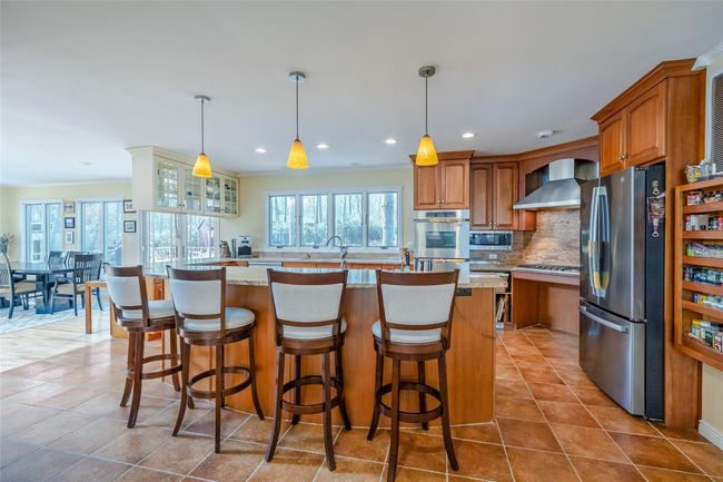 Kitchen featuring a sink, decorative backsplash, appliances with stainless steel finishes, wall chimney range hood, and brown cabinets | Image 12