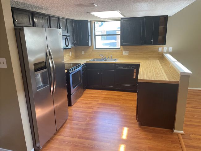 Kitchen featuring a textured ceiling, sink, light hardwood / wood-style floors, and black appliances | Image 7