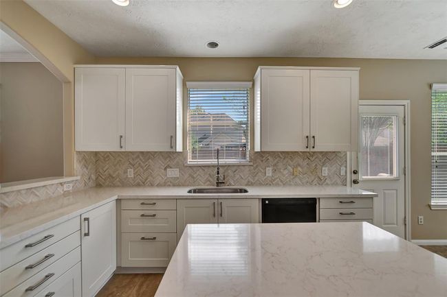This kitchen features a modern design with white cabinetry, a marble-look countertop, and a stylish herringbone backsplash. It has ample natural light, a sink overlooking a window, and a convenient door to the outside, making it both functional and inviting. | Image 21