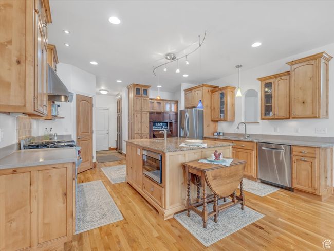 Kitchen with stainless steel appliances, a kitchen island with sink, a sink, light wood-style floors, and exhaust hood | Image 12