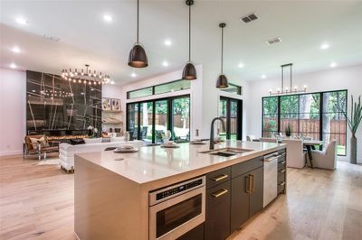 Kitchen featuring hanging light fixtures, stainless steel appliances, light hardwood / wood-style floors, and a kitchen island with sink | Image 3