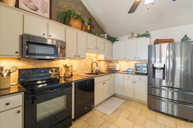 Kitchen featuring tasteful backsplash, a ceiling fan, white cabinets, black appliances, and a sink | Image 10