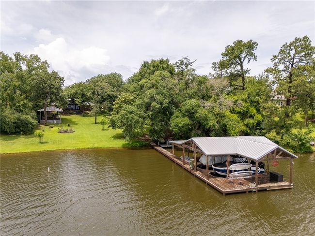 Dock area featuring boat lift, a water view, a lawn, and view of wooded area | Image 50