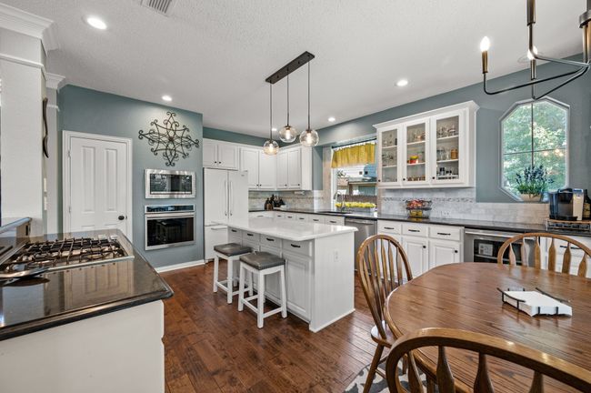Kitchen featuring white cabinets, pendant lighting, glass insert cabinets, dark wood-style floors, and stainless steel appliances | Image 11