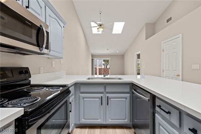 Kitchen featuring stainless steel appliances, a skylight, lofted ceiling, gray cabinetry, and a ceiling fan | Image 10