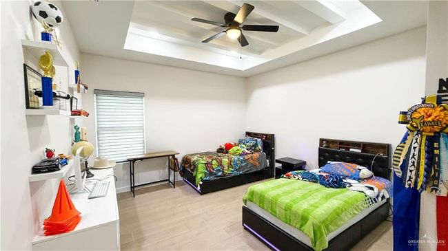 Bedroom with light wood-style flooring, a tray ceiling, and ceiling fan | Image 16