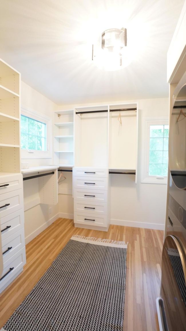 The jaw-dropping, newly added owners' walk-in closet is fully custom and boasts a ton of versatile storage options without hindering natural light. The white oak floors and new light fixture highlight both the cabinetry and LG wash tower. | Image 28