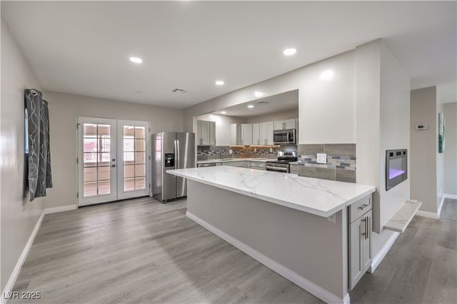 Kitchen with decorative backsplash, light wood-style flooring, light stone counters, stainless steel appliances, and french doors | Image 11