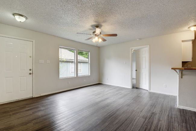 Unfurnished living room with ceiling fan, dark wood finished floors, a textured ceiling, and baseboards | Image 5