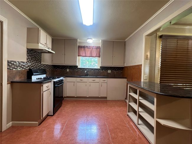Kitchen with black gas stove, under cabinet range hood, dark countertops, backsplash, and crown molding | Image 12