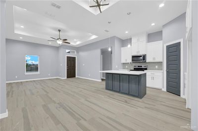 Kitchen with appliances with stainless steel finishes, white cabinets, a center island with sink, and light wood-type flooring | Image 3