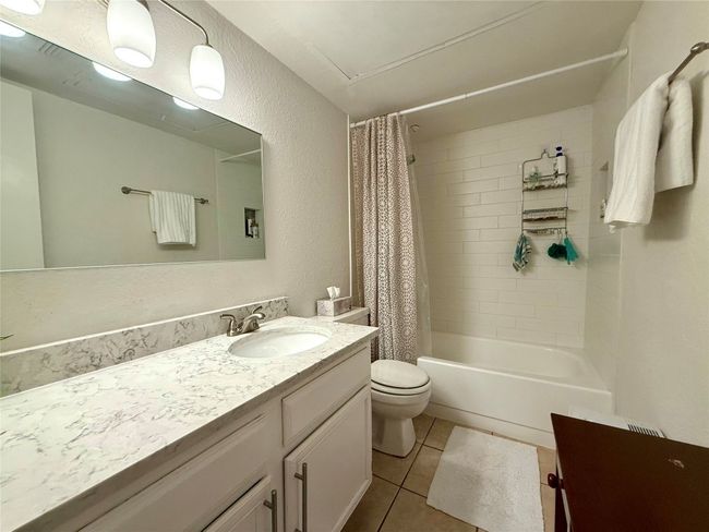 Bathroom featuring tile patterned flooring, shower / bathtub combination with curtain, toilet, a textured wall, and vanity | Image 16