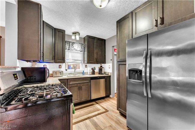 Kitchen featuring stainless steel appliances, a sink, light wood-style floors, light countertops, and a textured ceiling | Image 14