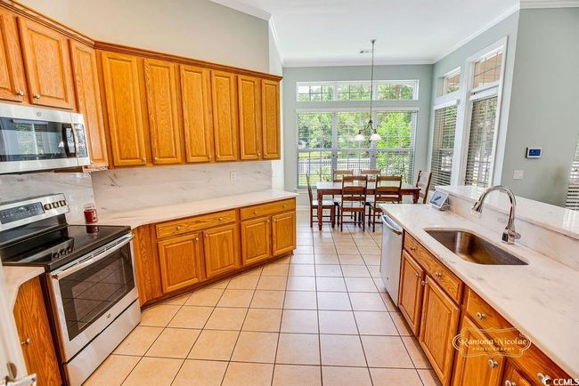 Kitchen with stainless steel appliances, crown molding, brown cabinets, decorative backsplash, and a chandelier | Image 12