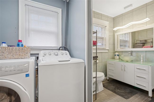 Washroom with a sink, tile walls, light wood finished floors, and washer and dryer | Image 21
