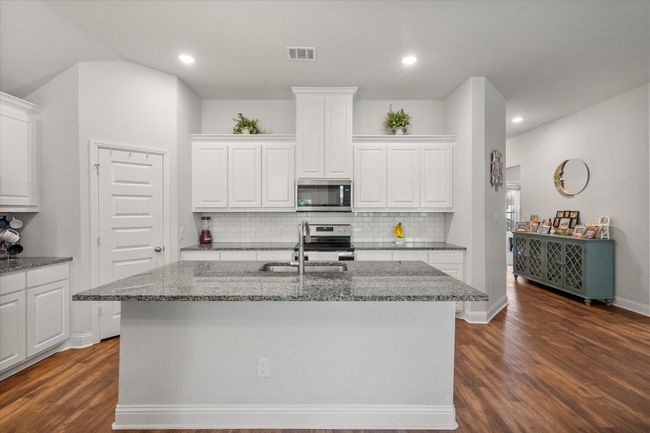 Kitchen with appliances with stainless steel finishes, dark wood finished floors, backsplash, white cabinets, and dark stone countertops | Image 9