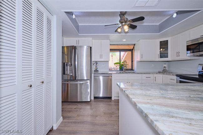 Kitchen with stainless steel appliances, a raised ceiling, dark wood finished floors, glass insert cabinets, and light stone countertops | Image 14