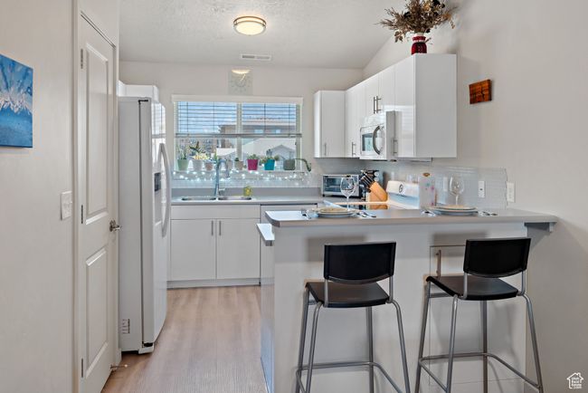 Kitchen featuring a peninsula, backsplash, white appliances, light wood-type flooring, and white cabinets | Image 6