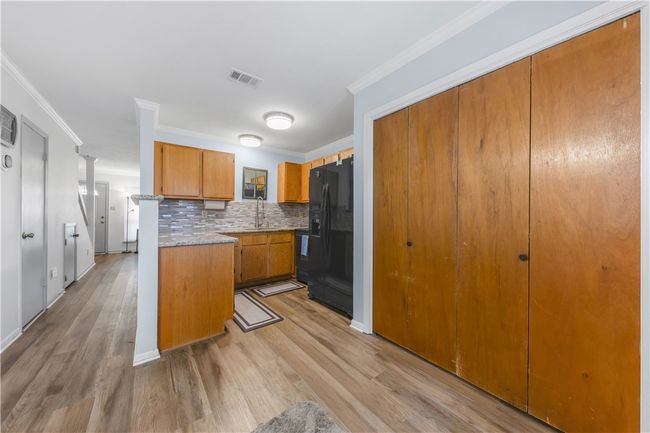 Kitchen featuring black fridge with ice dispenser, brown cabinets, light wood finished floors, decorative backsplash, and crown molding | Image 7