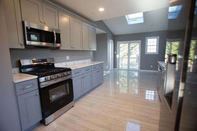 Kitchen with gray cabinetry, vaulted ceiling with skylight, light stone countertops, and appliances with stainless steel finishes | Image 11
