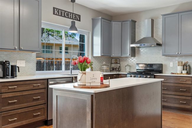 Kitchen with light countertops, backsplash, a center island, wall chimney range hood, and range with gas stovetop | Image 9