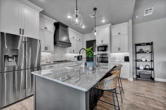 Kitchen with appliances with stainless steel finishes, premium range hood, decorative backsplash, white cabinets, and light stone counters | Image 18