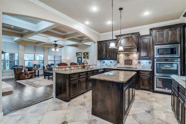 The 5 burner gas cooktop with a designer vent-a-hood and double ovens and a microwave provide all the appliances needed to prepare large meals. The large tile flooring is adorned with glass diamond decorative insets. | Image 16