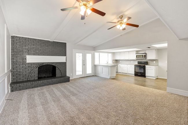 Unfurnished living room featuring vaulted ceiling with beams, a brick fireplace, baseboards, light colored carpet, and ceiling fan | Image 33