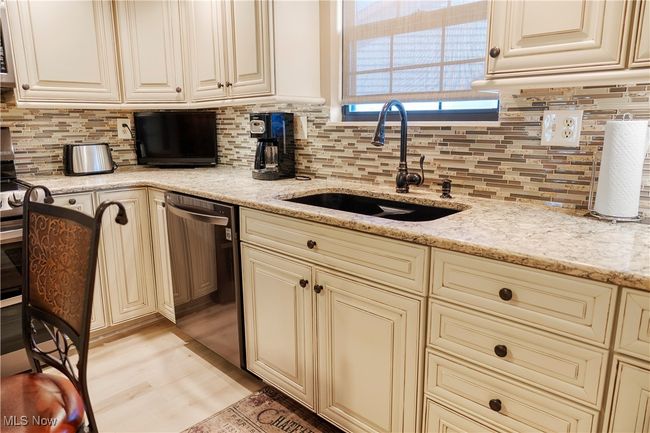 Kitchen featuring backsplash, dishwashing machine, cream cabinetry, and a sink | Image 12